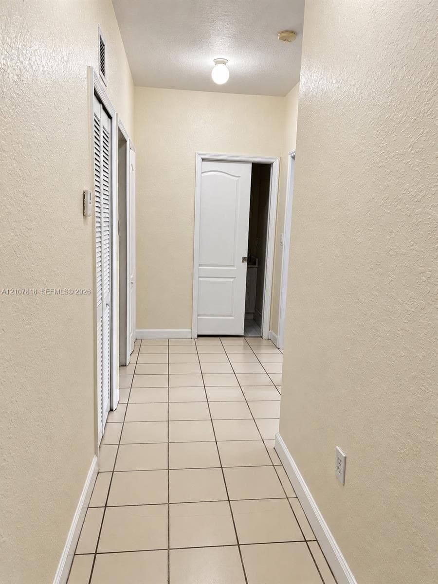 Hallway featuring ceramic tile flooring, neutral wall finishes, white six-panel interior doors, and louvered closet doors