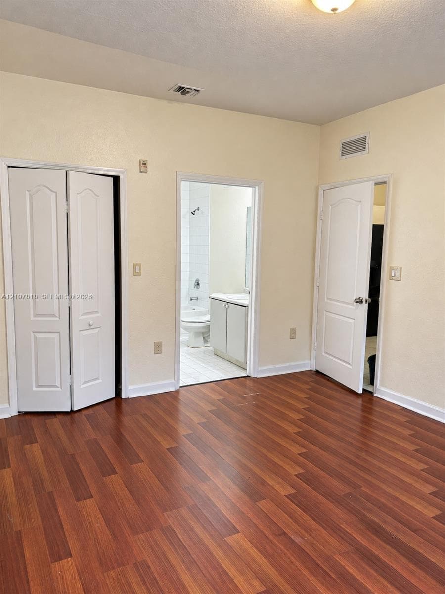 Room featuring wood-finish flooring, white paneled interior doors, and built-in closet storage