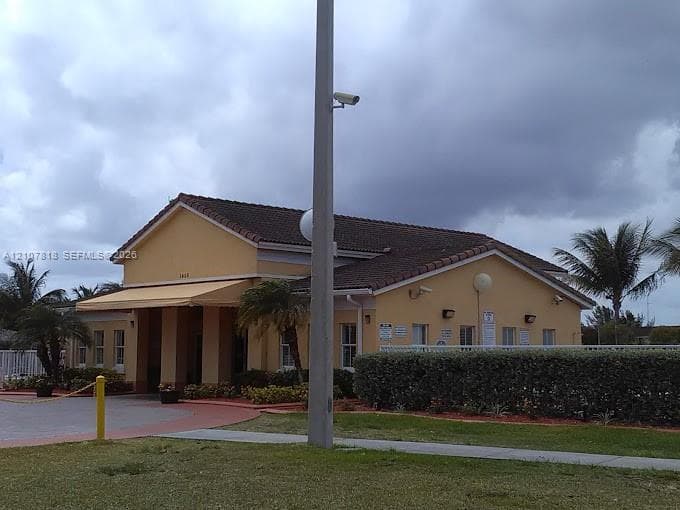 Single-story structure featuring a tiled roof, stucco exterior, covered entryway, and exterior security lighting