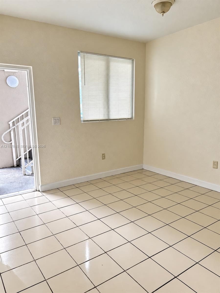 Neutral-toned room featuring tile flooring, a window equipped with horizontal blinds, and a semi-flush mount ceiling fixture