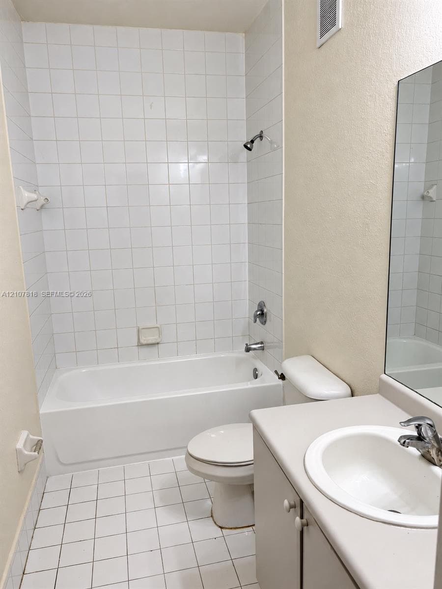 Bathroom featuring a tub-shower combination with floor-to-ceiling white tile surround, ceramic tile flooring, a vanity with a solid-surface integrated sink, and a full-width wall mirror