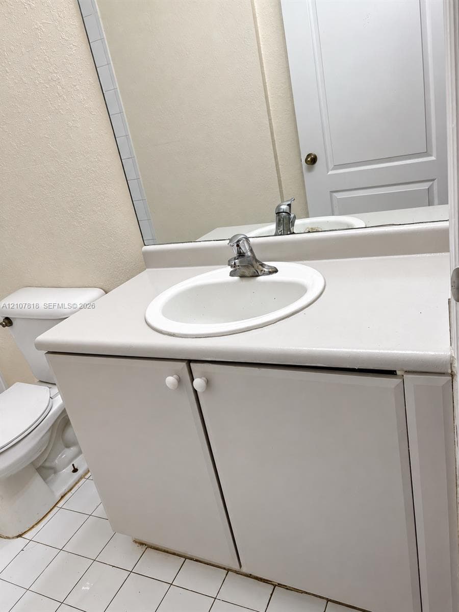 Bathroom vanity with a solid-surface integrated sink, chrome faucet, white cabinetry, and square ceramic tile flooring