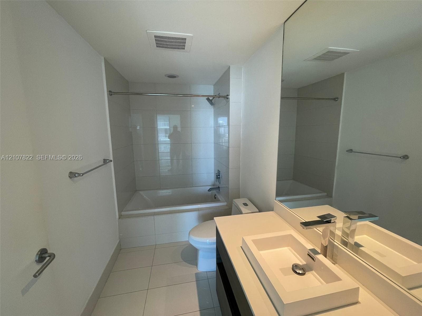 Modern bathroom featuring a vanity with a rectangular vessel sink, polished metal faucet, full-width wall mirror, and a tub with tiled surround