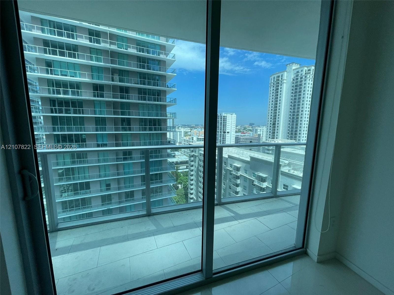 Floor-to-ceiling sliding glass door, private balcony with glass railing, and large-format tile flooring