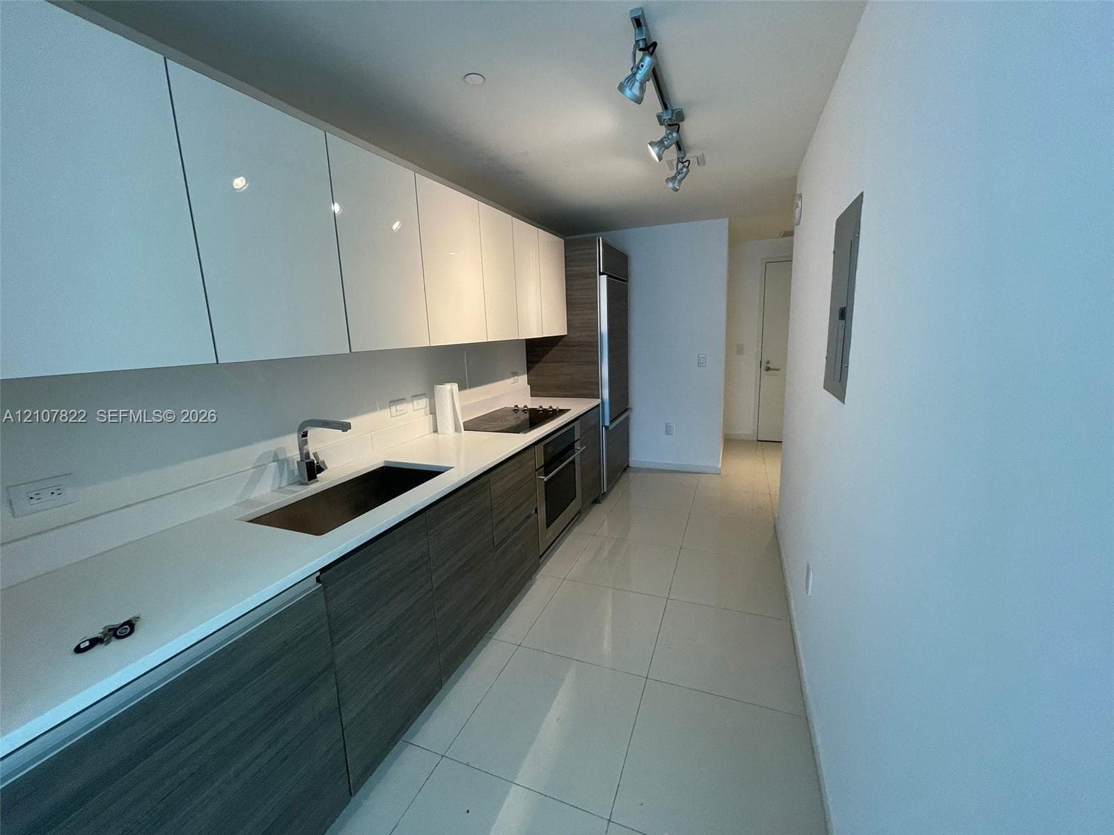 Kitchen featuring high-gloss white upper cabinetry, wood-finish lower cabinetry, stone-surface countertops, integrated stainless steel appliances, and polished tile flooring