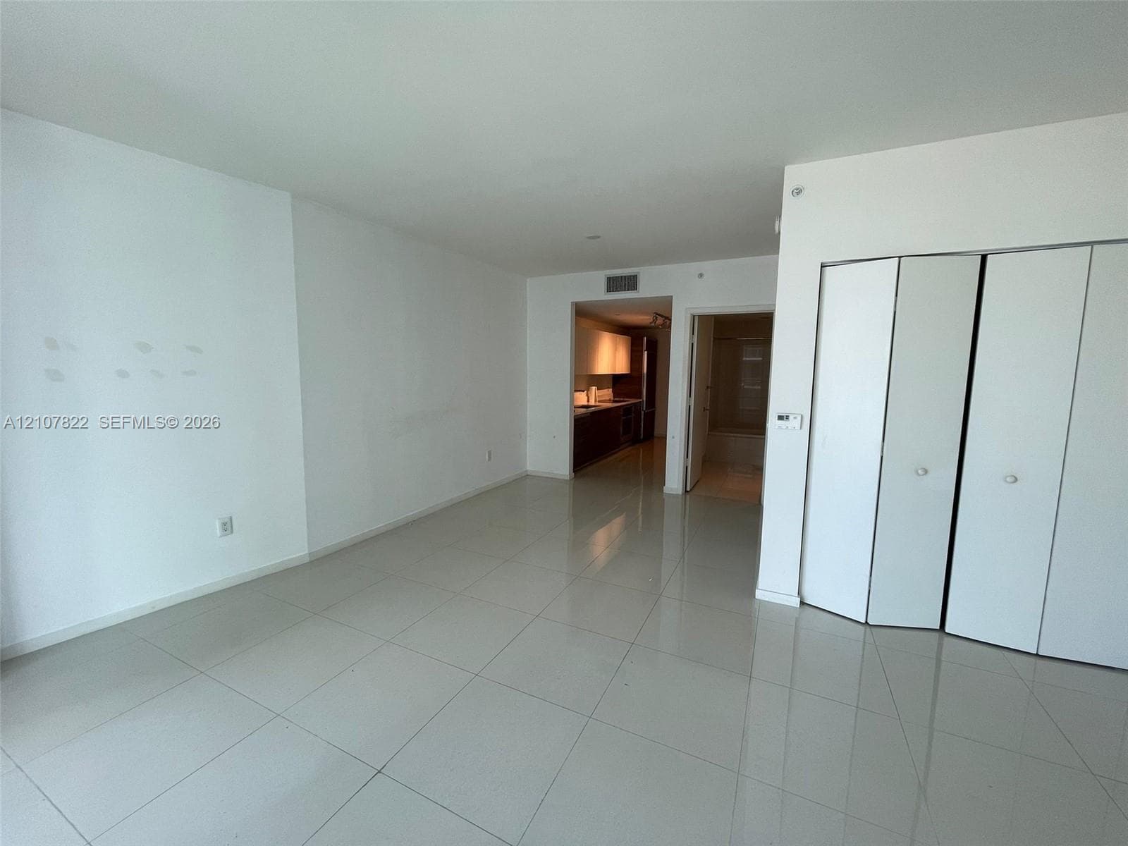 Open interior space featuring light-toned tile flooring, white walls, and triple-panel bi-fold closet doors