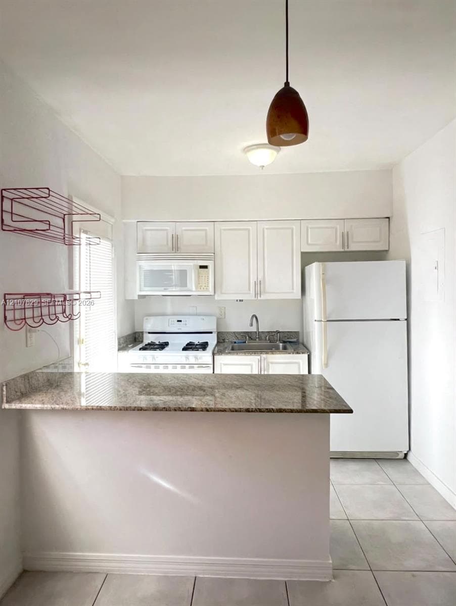 Kitchen featuring a stone-topped breakfast bar, white shaker-style cabinetry, a white gas range, and a drop-down pendant light