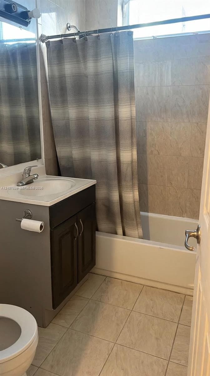 Bathroom featuring a single-sink vanity with cabinet storage, a tub-shower combination with tiled surround, and large-format floor tiling