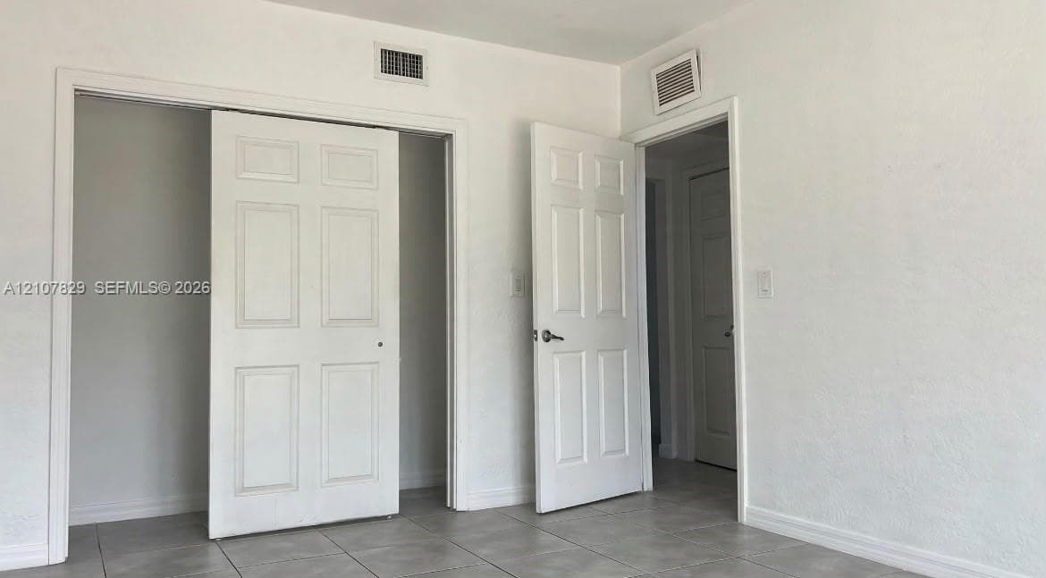 Neutral-toned interior space featuring light-colored tile flooring, smooth wall finishes, and multiple six-panel interior doors