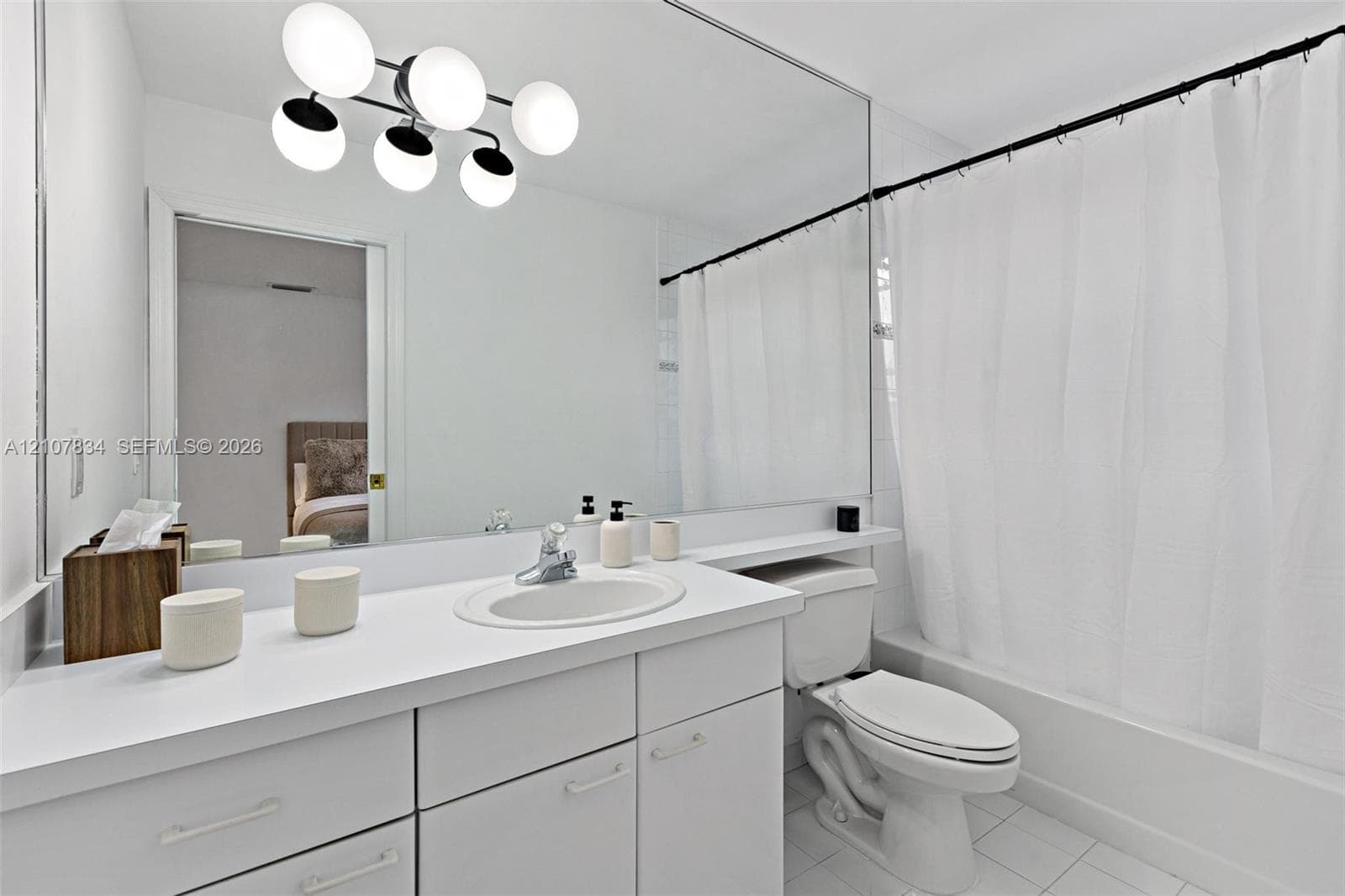 Bathroom featuring white cabinetry, integrated countertop with an oval basin, large wall-to-wall mirror, multi-globe light fixture, and a tub-shower combination