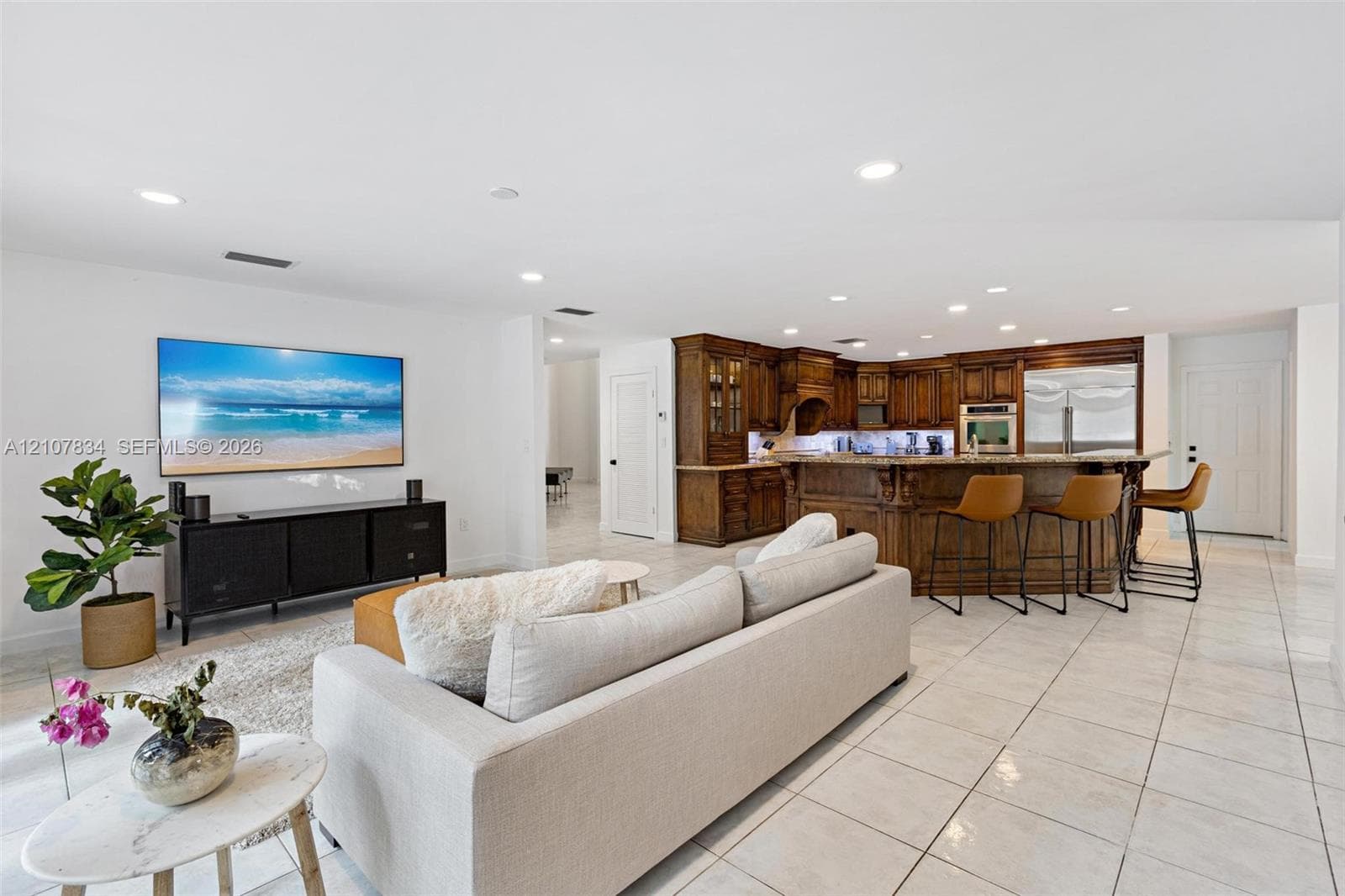 Open-concept living space featuring ceramic tile flooring, recessed lighting, and a kitchen equipped with dark wood-finish cabinetry, a curved breakfast bar, and built-in stainless steel appliances