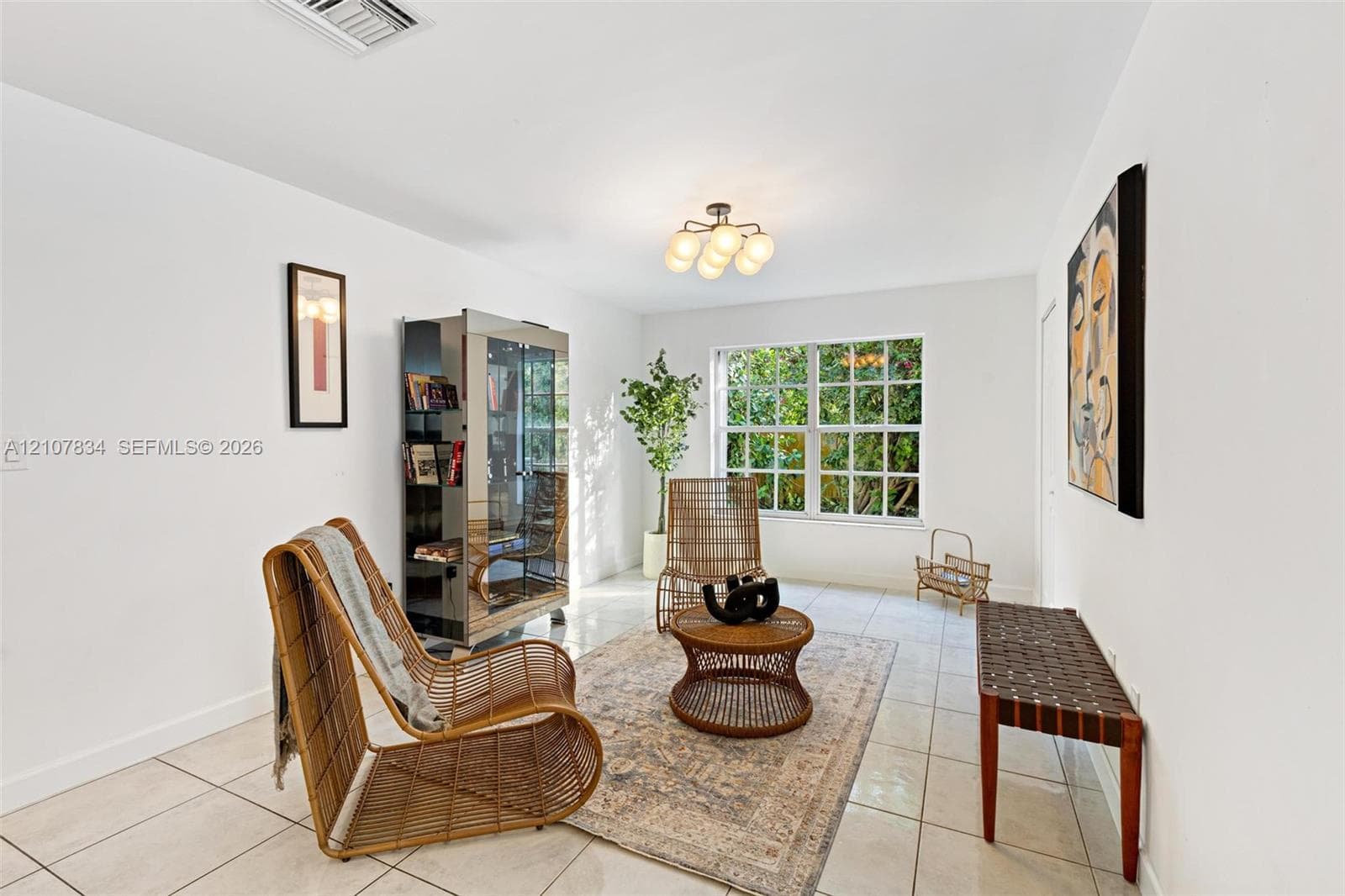 Bright interior space featuring polished tile flooring, multi-pane window with exterior greenery, and a multi-bulb flush-mount light fixture
