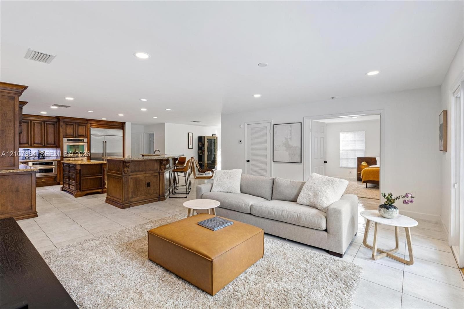 Kitchen featuring custom wood cabinetry, stone countertops, a large center island, and recessed ceiling lighting throughout the main living area with large-format floor tile