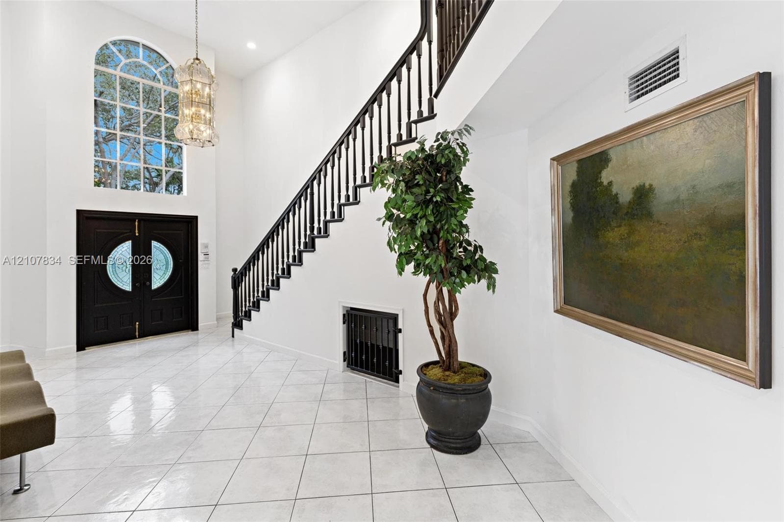 Foyer featuring double entry doors with decorative glass inlays, high ceilings, large arched window, tile flooring, and a staircase with a dark-finish metal railing