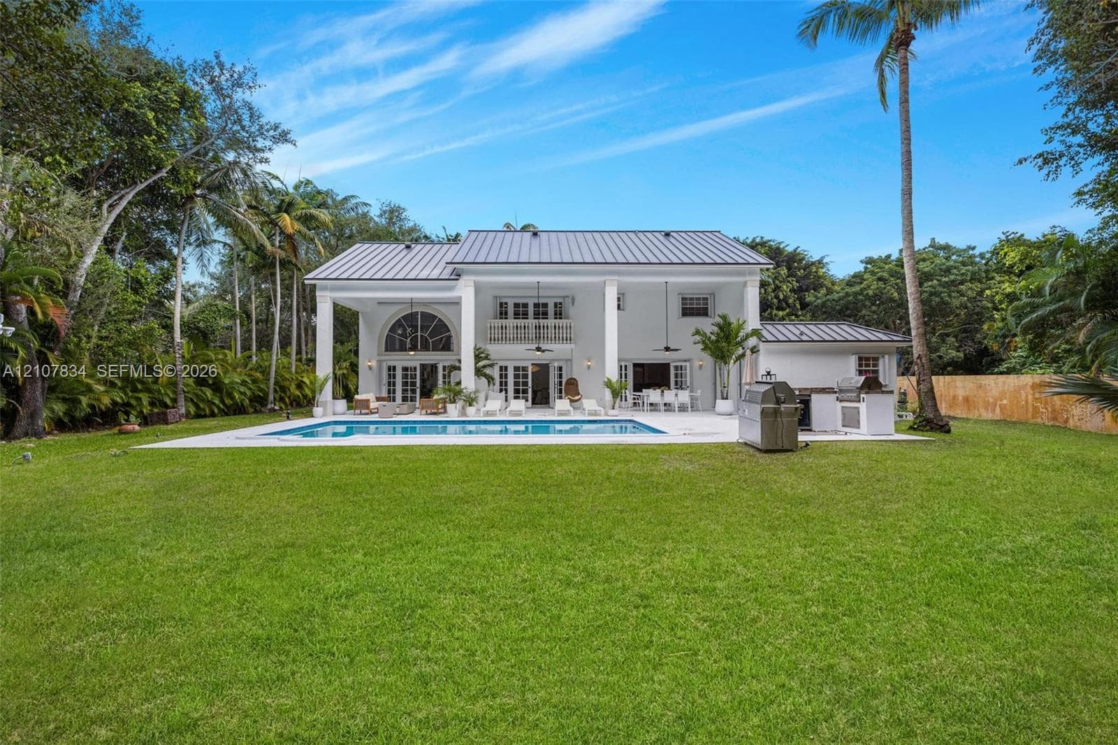 Rear exterior featuring a metal roof, covered patio with recessed lighting, in-ground pool, expansive lawn, and built-in outdoor kitchen station