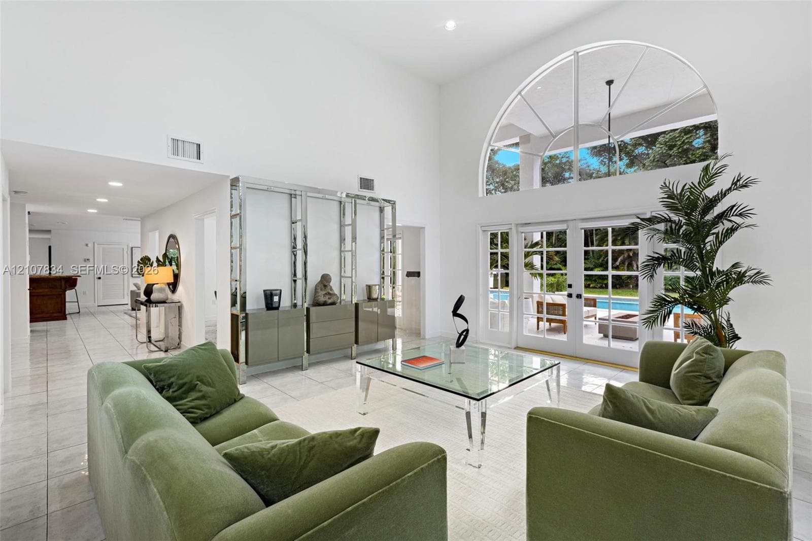 Double-height living area featuring floor-to-ceiling windows, arched transom window, large-format tile flooring, and custom built-in shelving