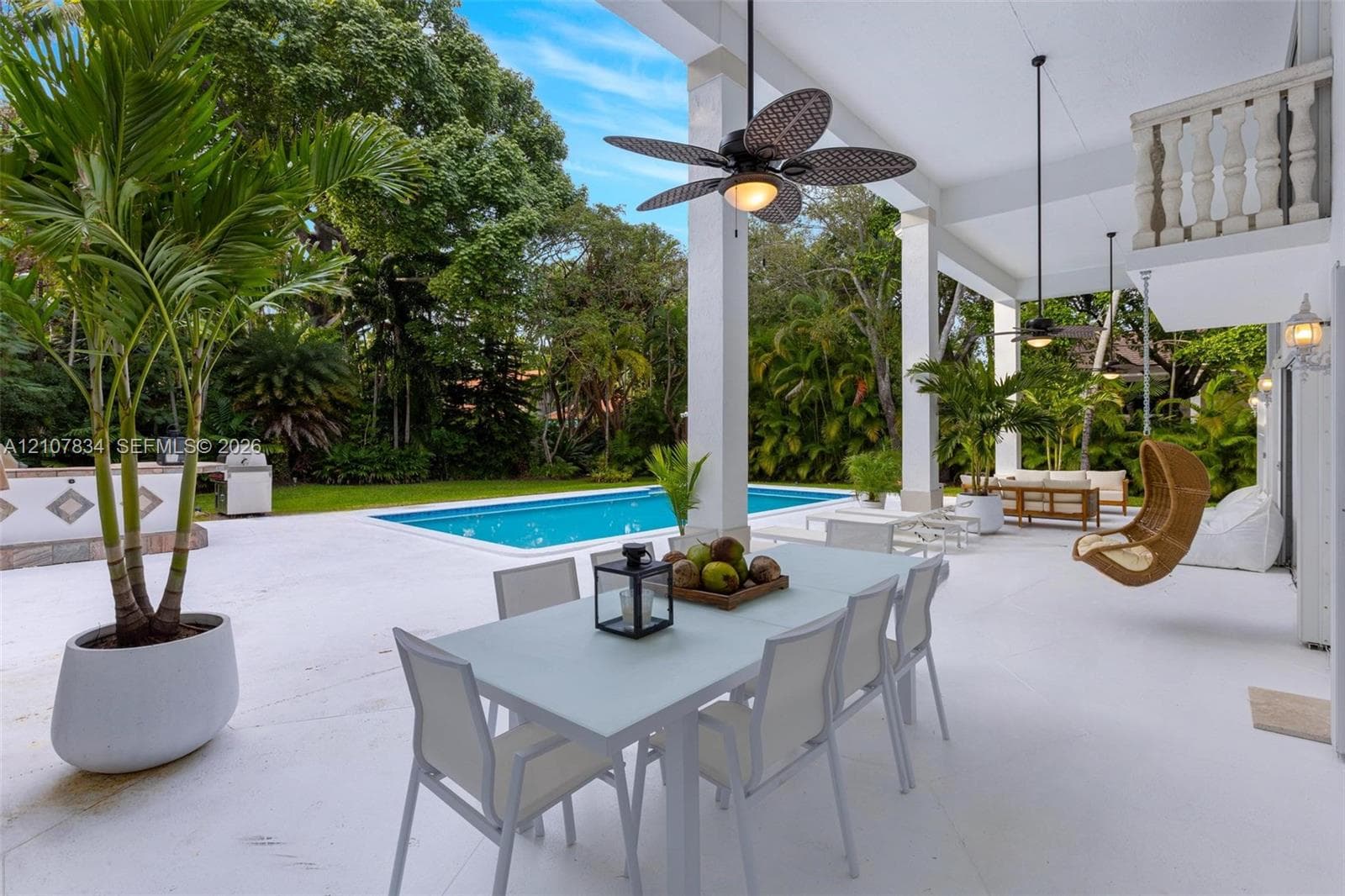Covered patio featuring a swimming pool, integrated outdoor kitchen, stone-finish balustrade, and ceiling-mounted fans