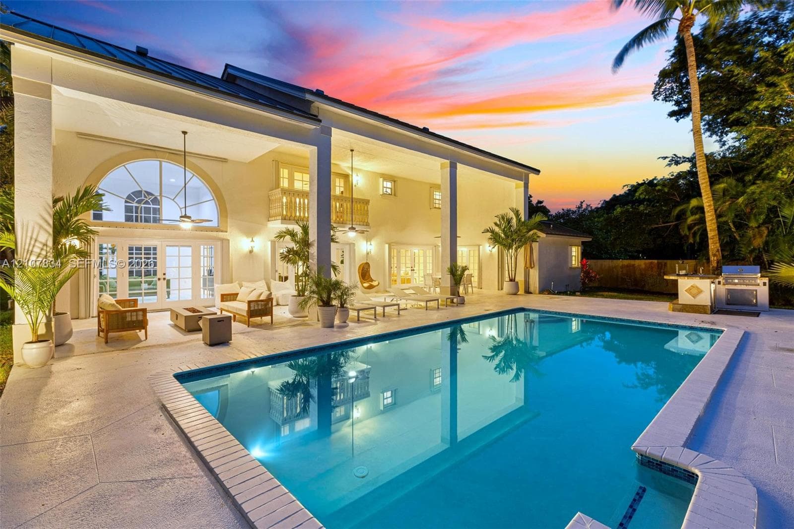 Covered patio featuring an expansive concrete deck, in-ground swimming pool, built-in outdoor kitchen with grill, and arched window details