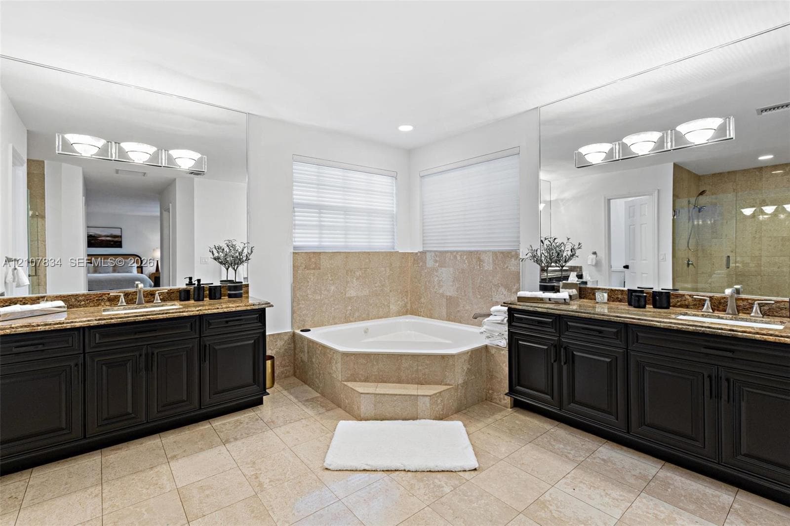 Dual vanity featuring dark cabinetry, stone countertops, and undermount sinks, complemented by a stone-surround corner soaking tub and a glass-enclosed shower