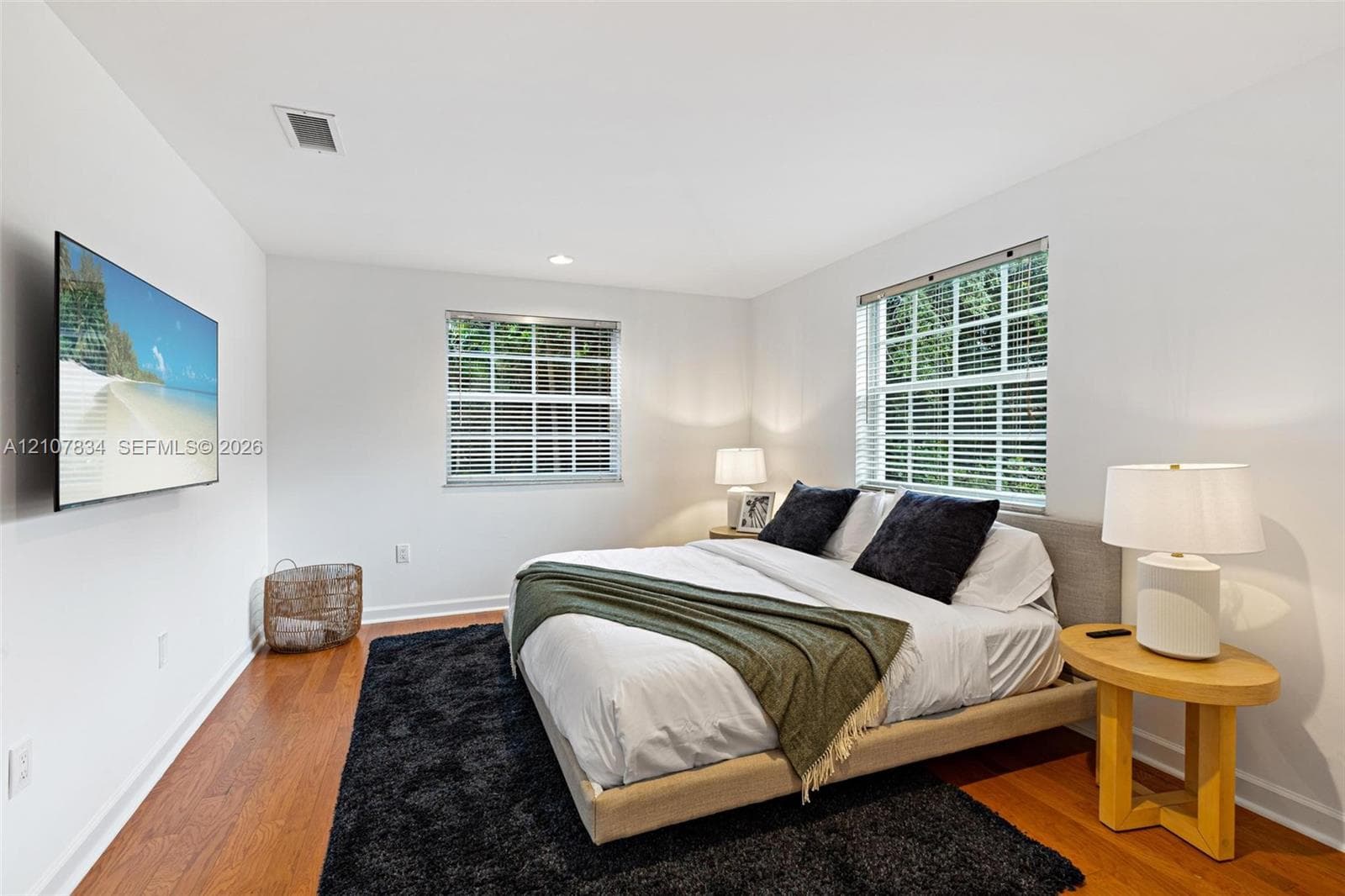 Bright bedroom featuring wood-finish flooring, two multi-pane windows with integrated blinds, and recessed lighting