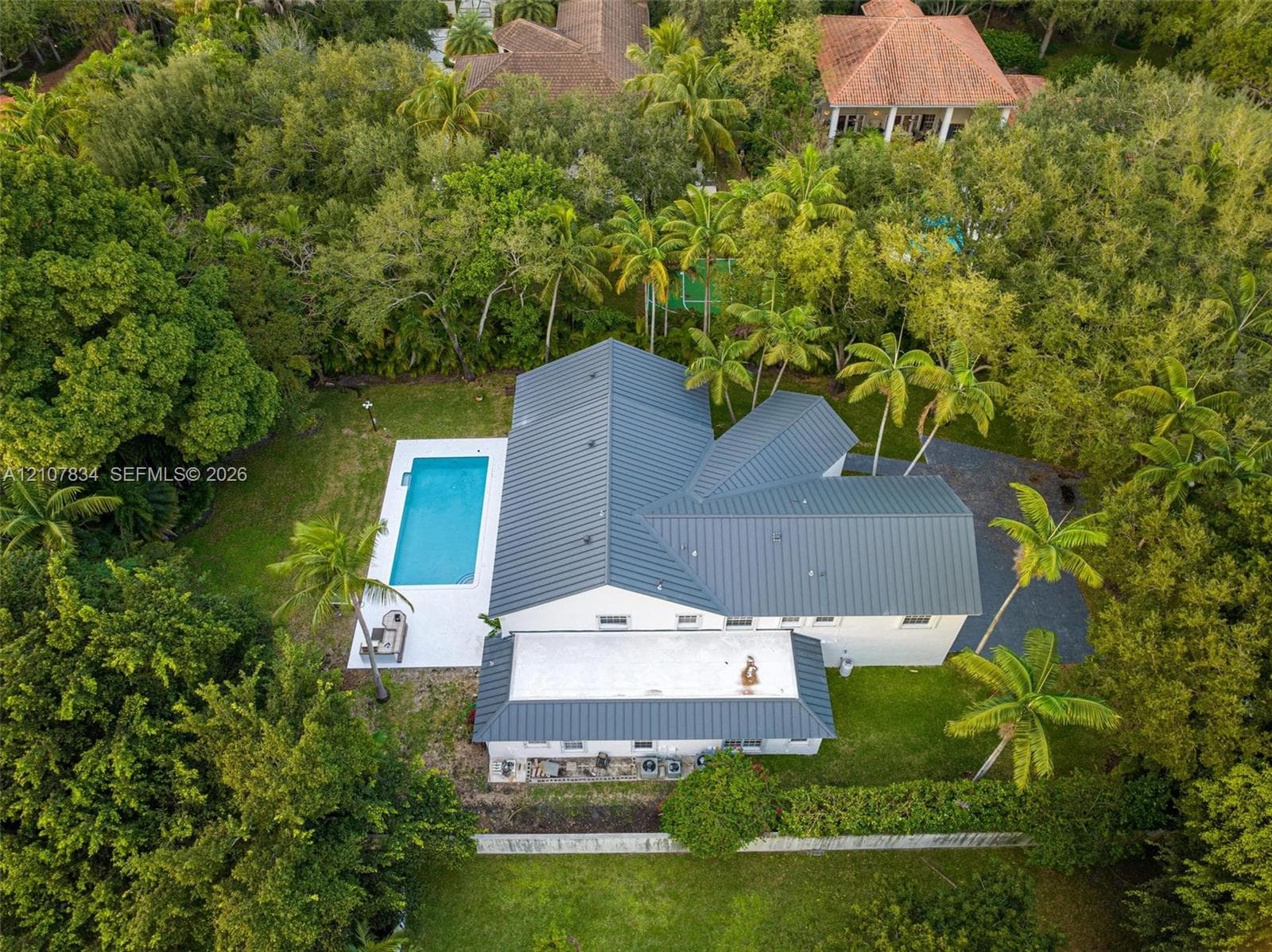 Aerial perspective of the property featuring a standing seam metal roof, an in-ground swimming pool, concrete pool deck, and mature landscaping