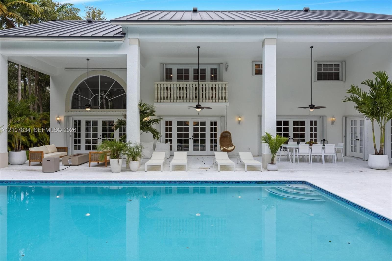 Covered patio with integrated ceiling fans, in-ground swimming pool, second-story balcony with balustrade, multiple sets of multi-lite glass doors, and smooth stone pool decking