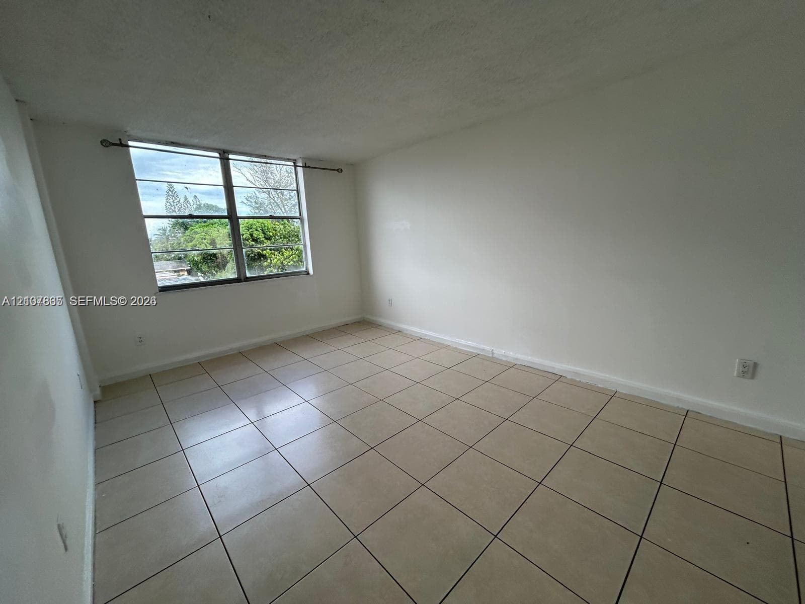 Interior space featuring neutral wall-to-wall tile flooring, smooth white walls, and a large metal-framed window