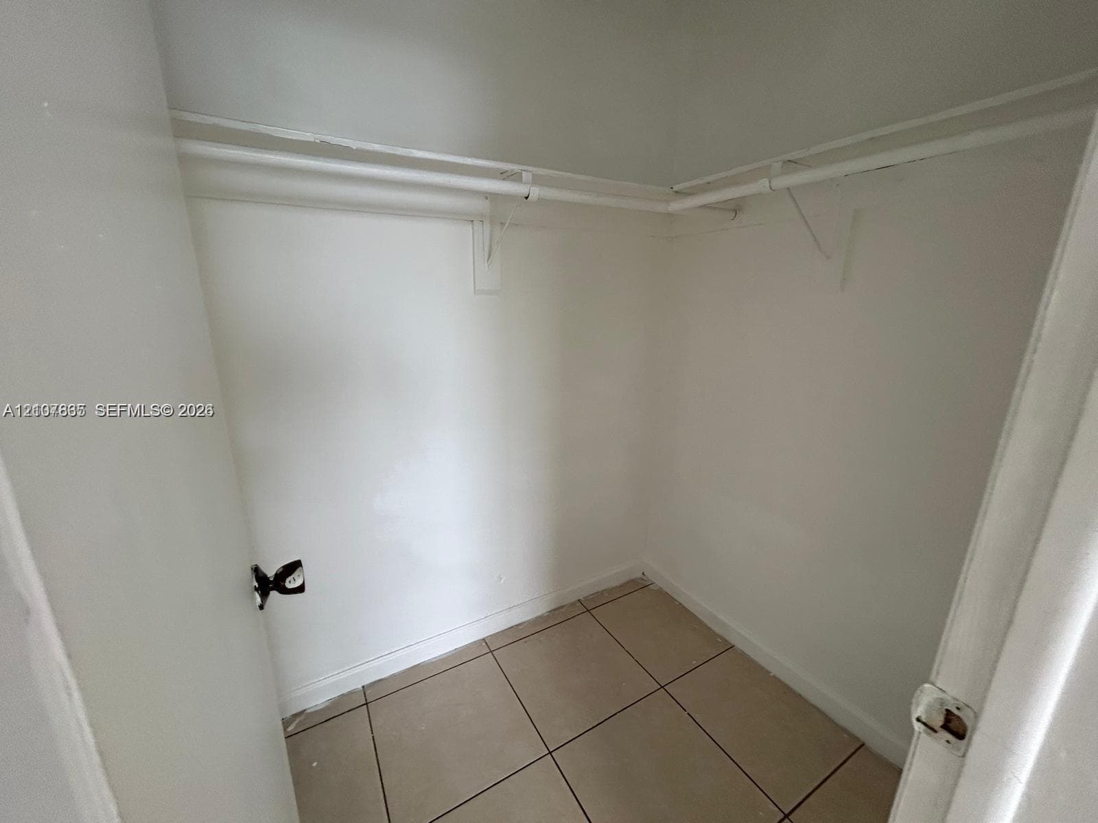 Storage space featuring large-format ceramic tile flooring, neutral wall finishes, and mounted white shelving rods