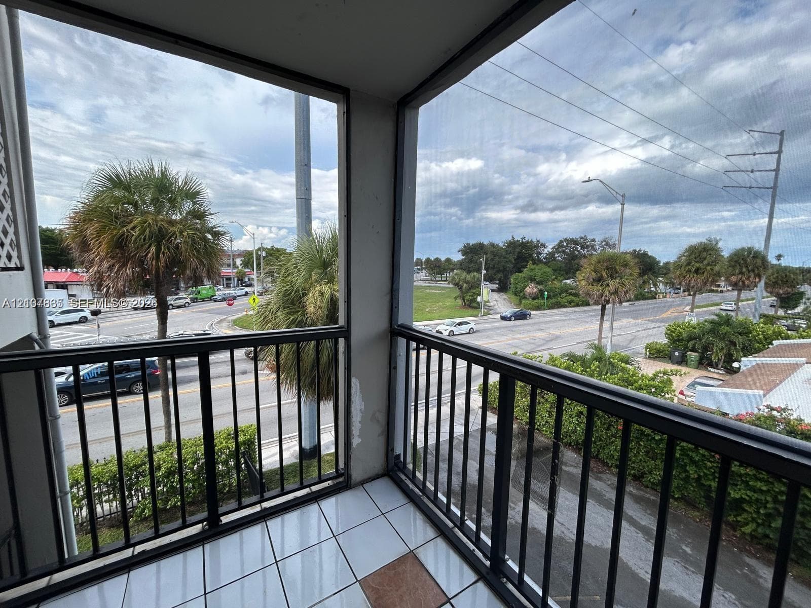 Covered balcony featuring screen enclosure, black metal railings, and tile flooring