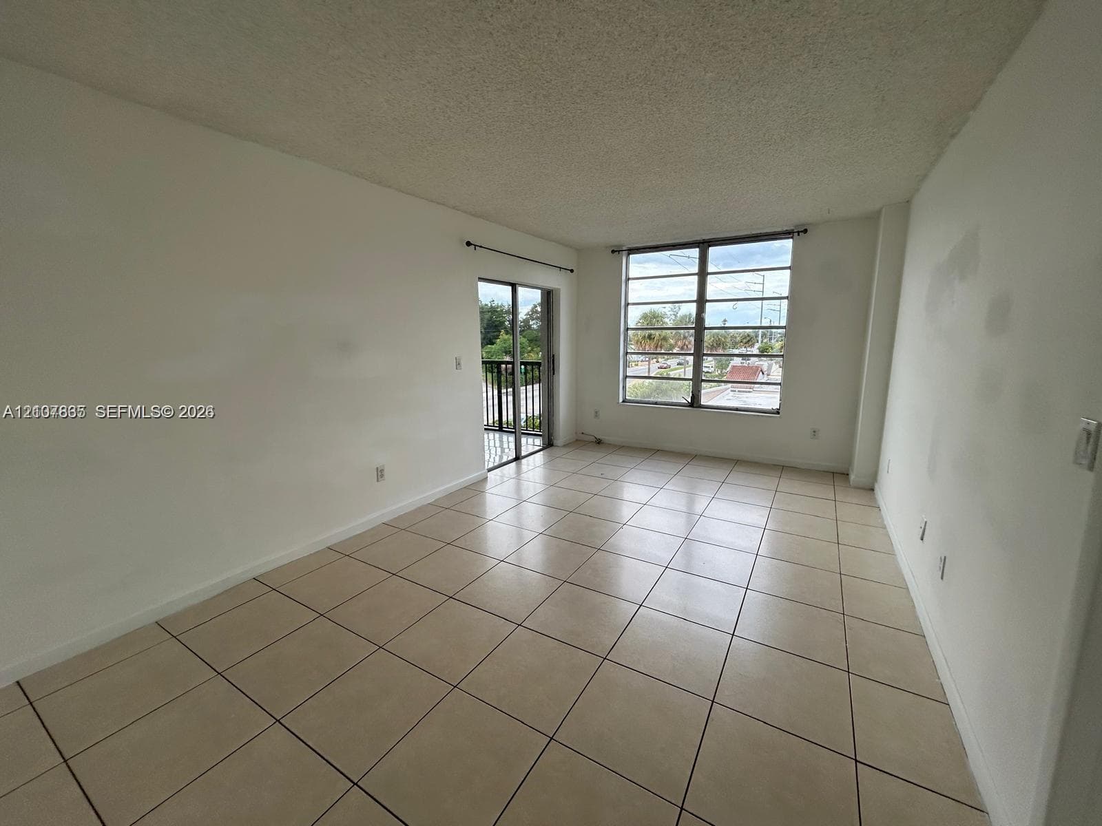 Neutral-toned ceramic tile flooring, large multi-pane windows, and a sliding glass door providing external access to a railed balcony