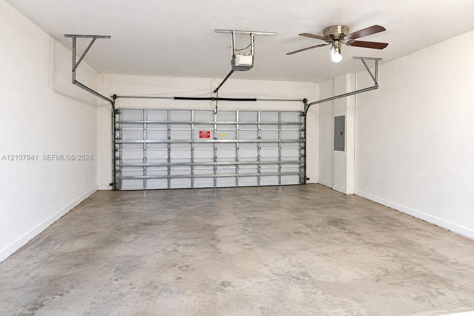 Two-car garage featuring a reinforced steel sectional door, concrete flooring, an automated overhead door opener, and a ceiling-mounted light fixture with fan