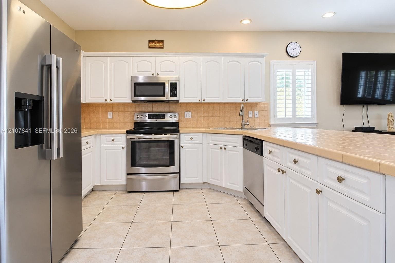 Kitchen featuring white cabinetry, stainless steel appliances, tile countertops, tile backsplash, and tile flooring