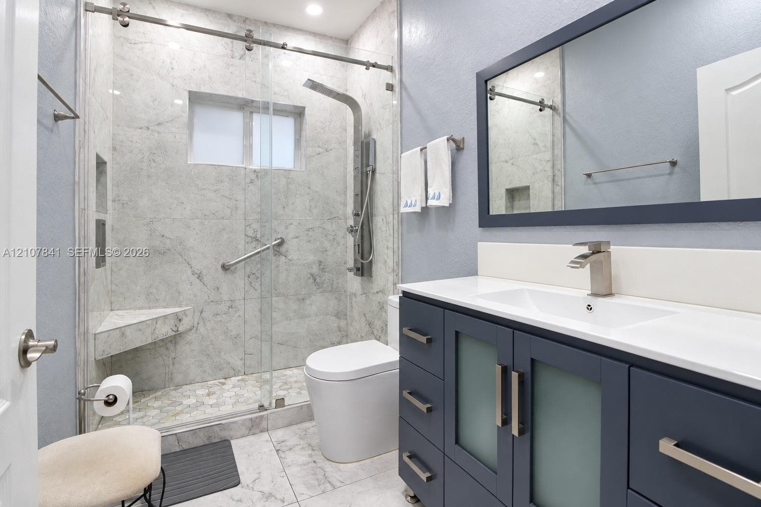 Bathroom featuring a vanity with blue cabinetry, a rectangular sink, stone-surround shower with a glass sliding door, and a built-in shower seat