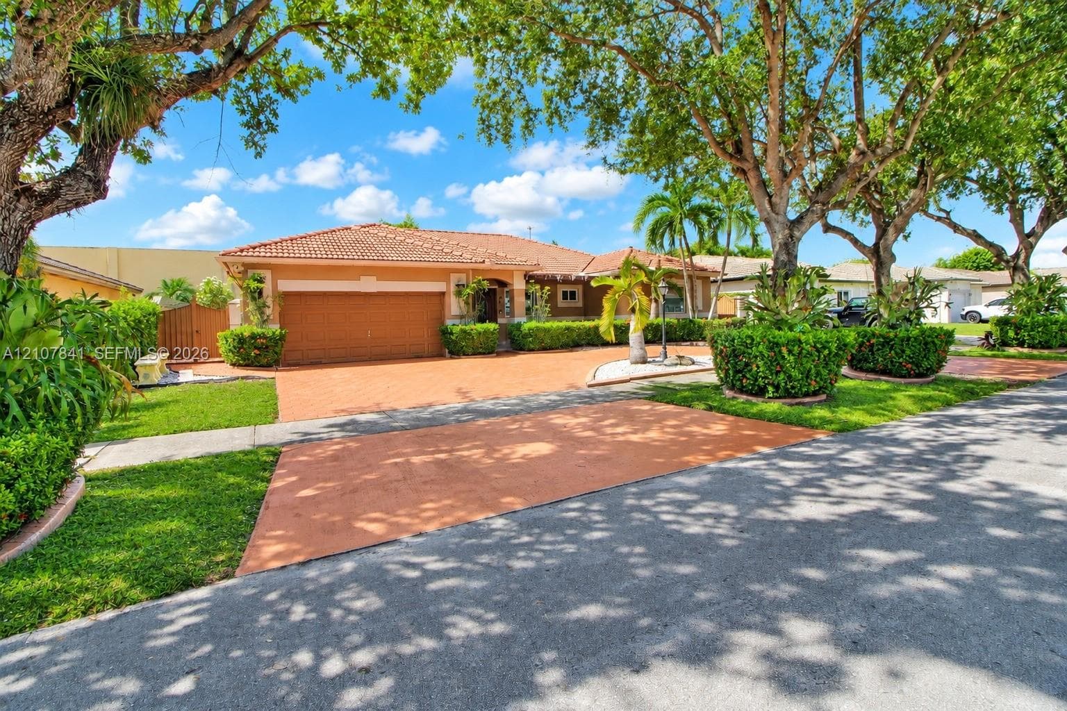 Single-story residence featuring a tiled roof, expansive paved driveway, multi-car garage, and established landscaping with mature trees