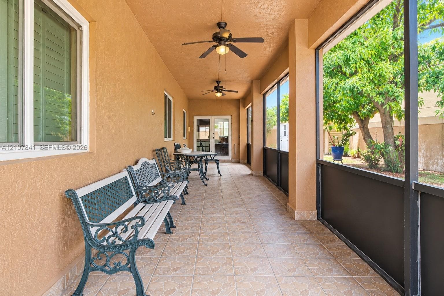 Screened-in lanai featuring tile flooring, dual ceiling fans, stucco exterior walls, and a multi-pane glass entry door