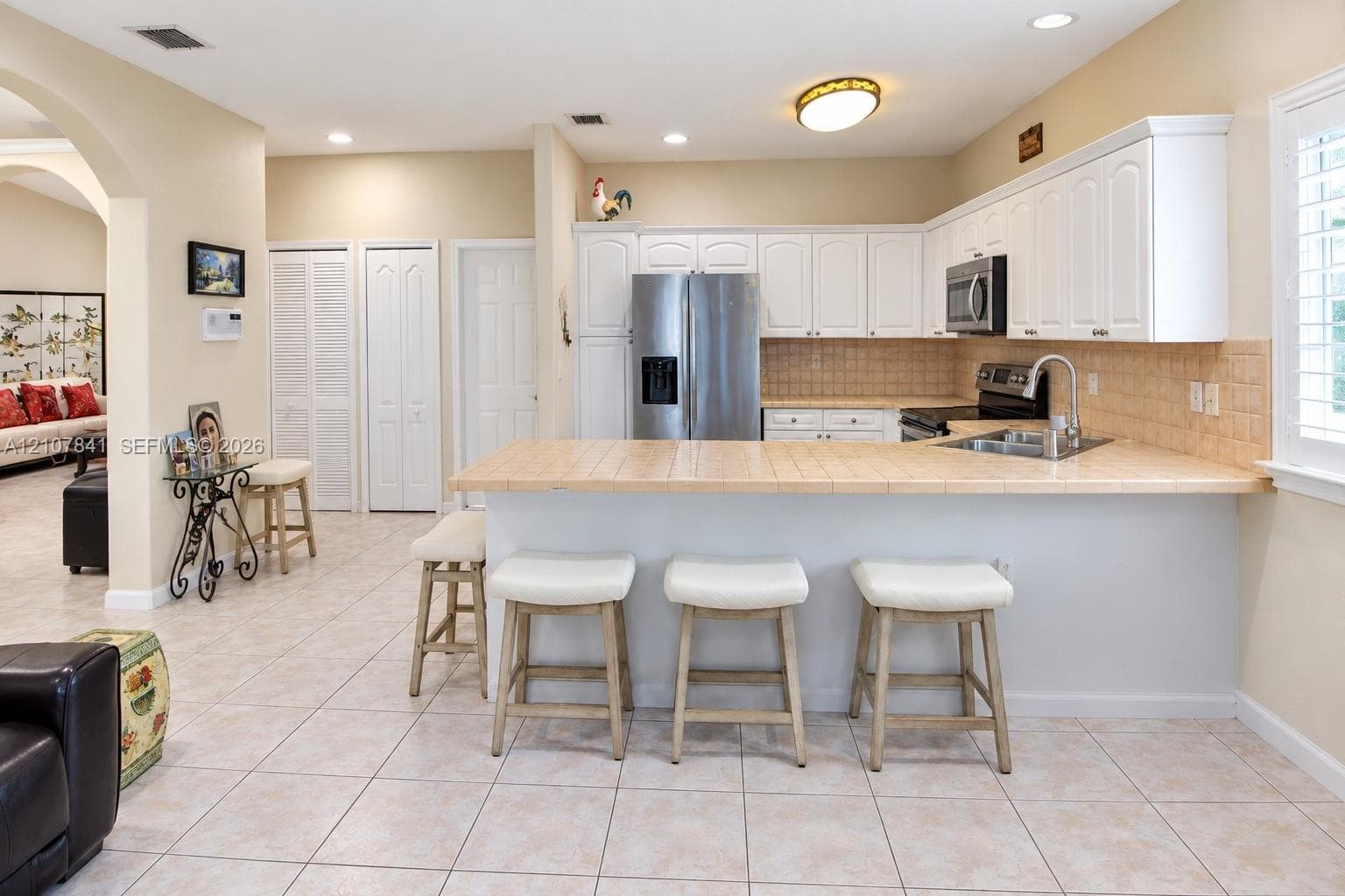 Kitchen featuring white shaker-style cabinetry, tiled countertops, stainless steel appliances, recessed lighting, and tile flooring