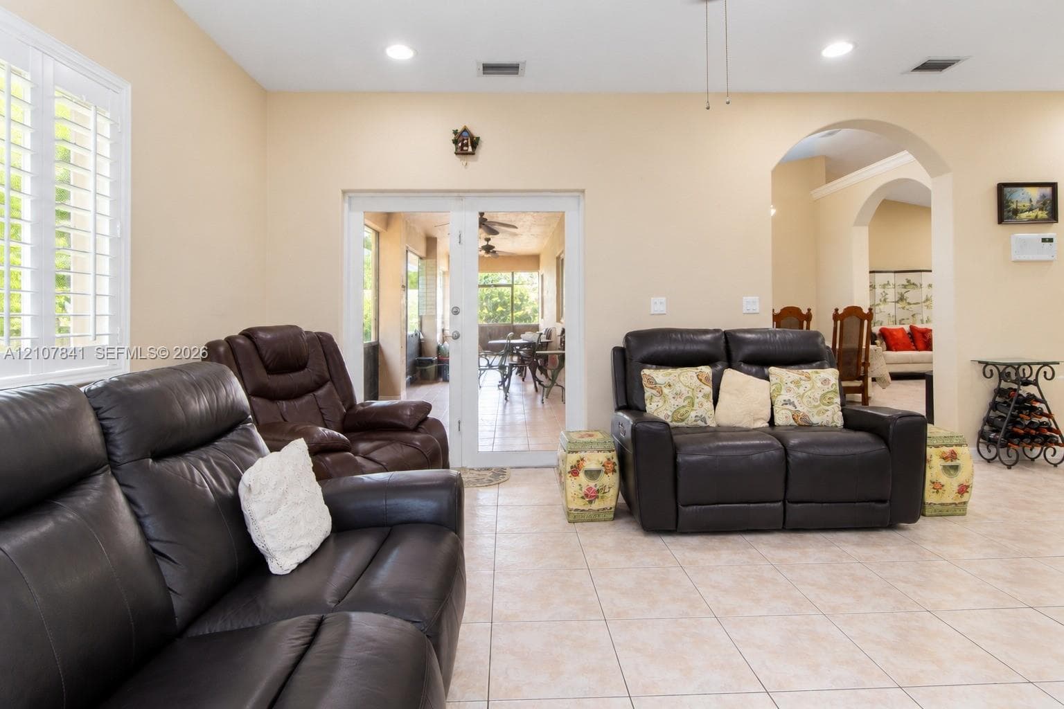 Neutral interior featuring light tile flooring, recessed lighting, plantation shutters, and an arched entryway with double-door access to an exterior screened enclosure