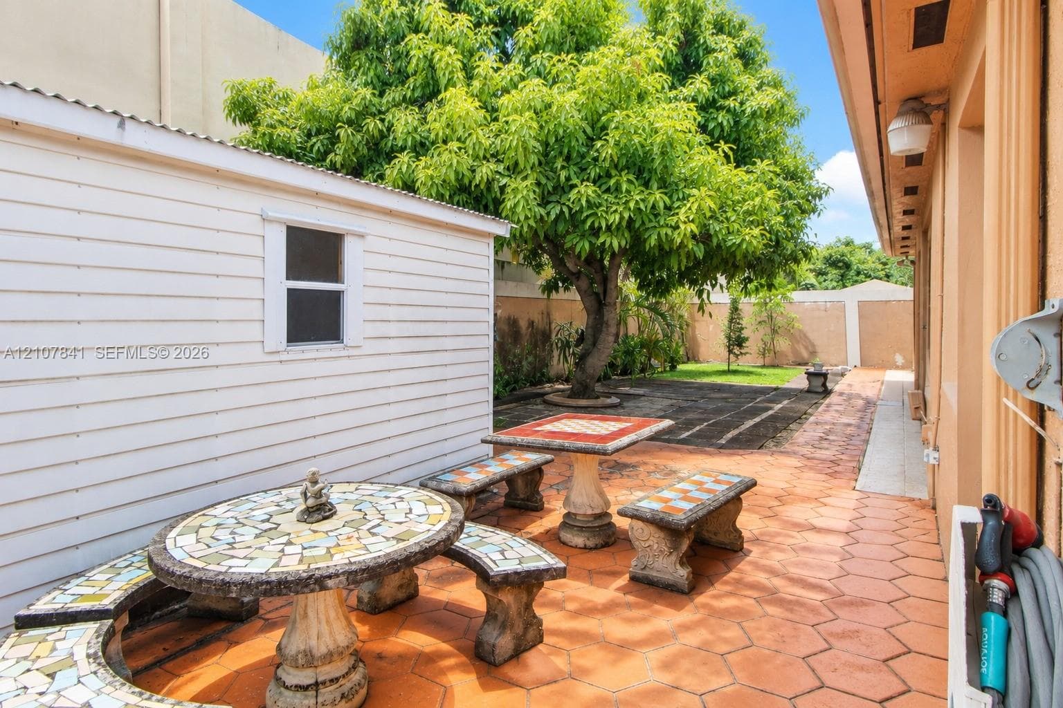 Outdoor patio featuring hexagonal tile flooring, a detached structure with horizontal siding, and a mature shade tree
