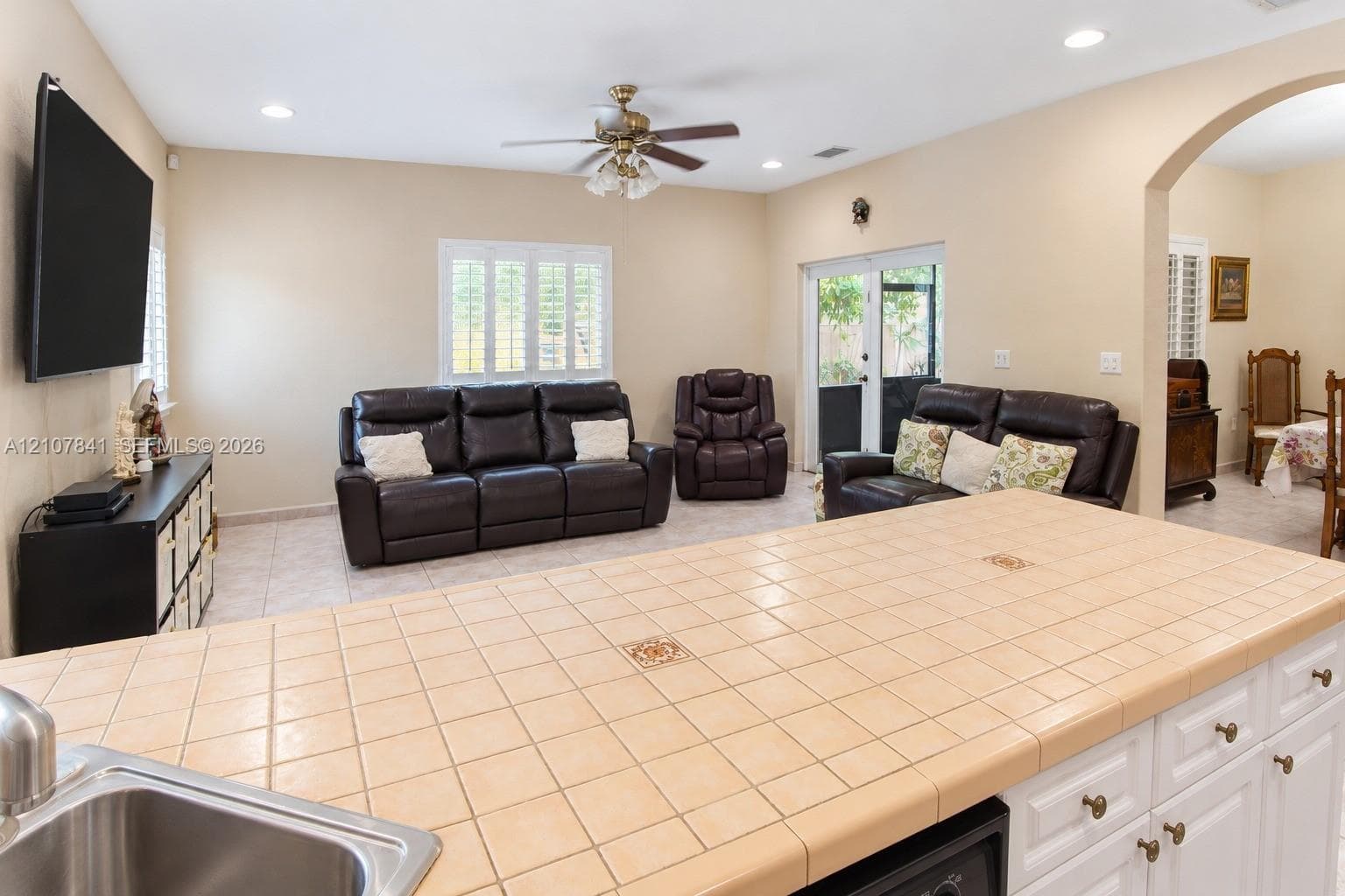 Kitchen island featuring ceramic tile countertops with decorative inlays, white cabinetry, integrated stainless steel sink, tile flooring, and recessed ceiling lighting