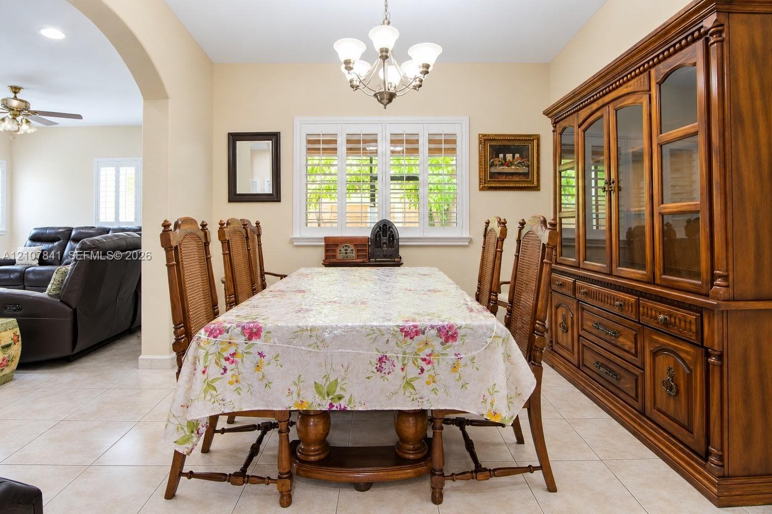 Dining area featuring tile flooring, arched entry, custom window shutters, and a central multi-light chandelier