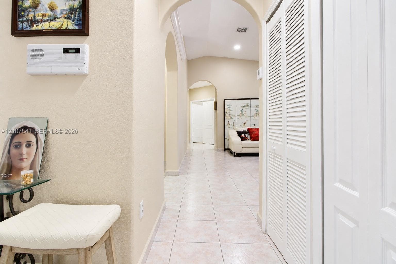 Hallway featuring arched architectural openings, neutral ceramic tile flooring, and white louvered-style closet doors