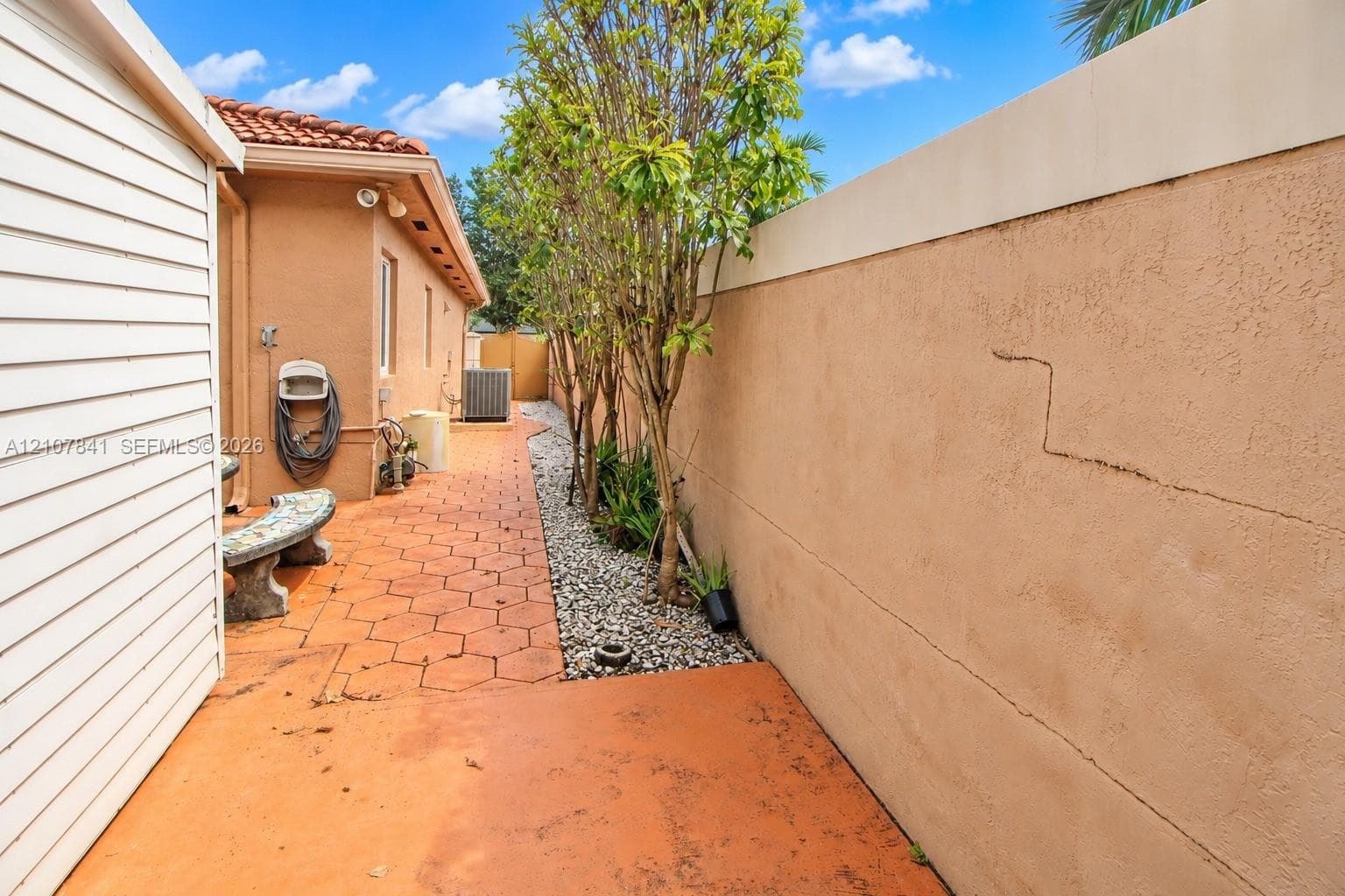 Side patio featuring hexagonal pavers, a perimeter masonry wall, stone ground cover, and mature landscape plantings
