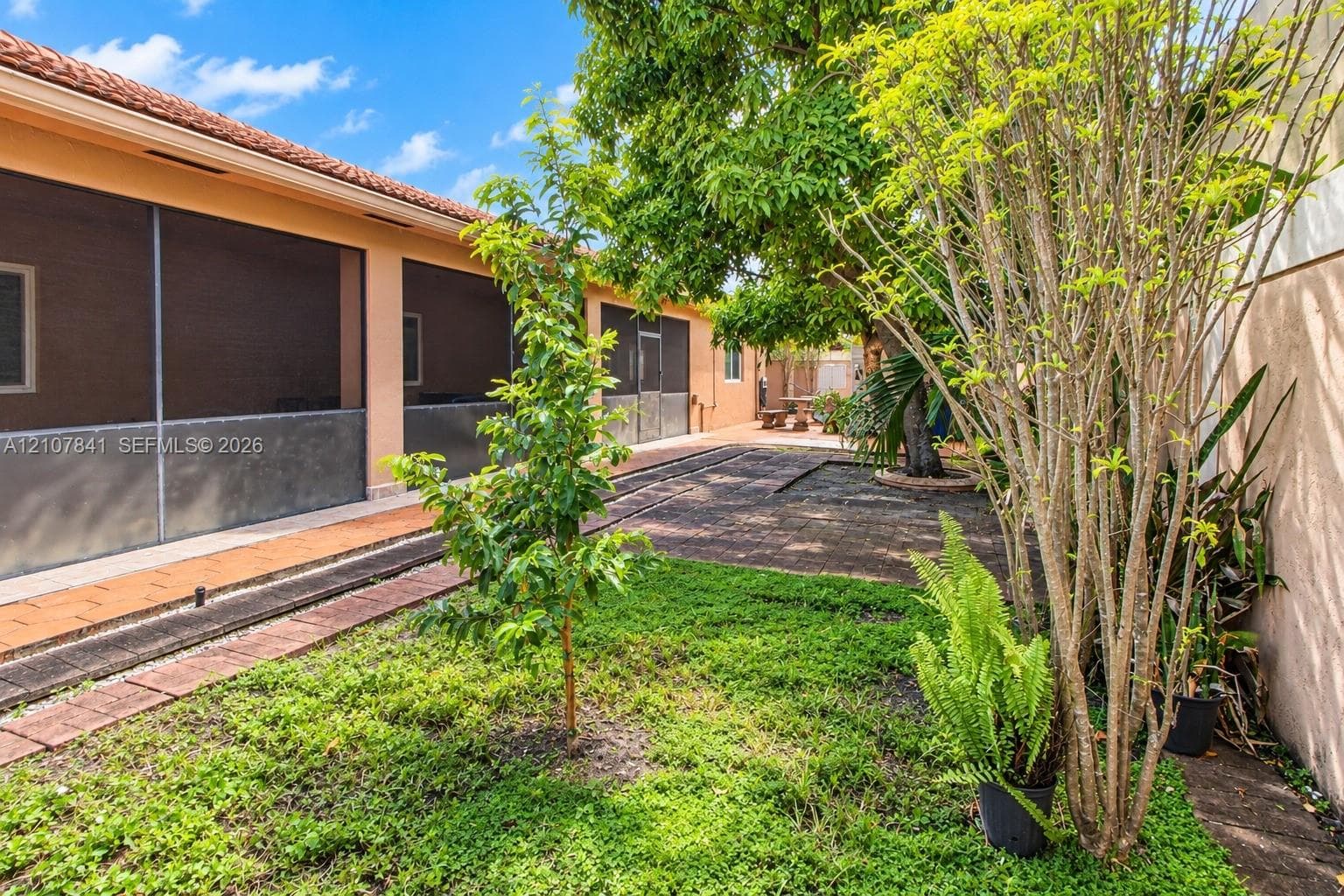 Screened-in rear porch with terracotta-style tile flooring, mature landscaping, and concrete perimeter wall