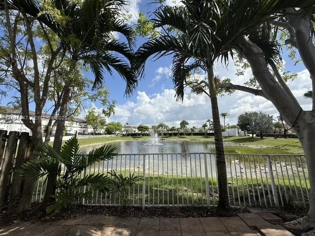 Outdoor brick patio featuring a metal fence enclosure, mature palm trees, and a pond with a central fountain