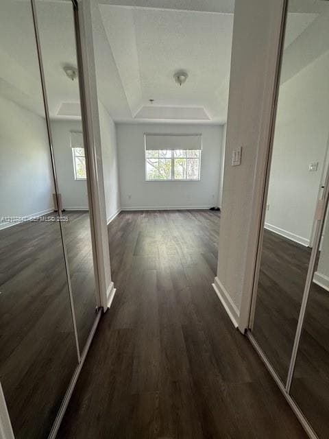 Room featuring wood-finish flooring, a tray ceiling, dual mirrored sliding closet doors, and a window with a roller shade