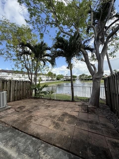 Rear patio featuring stone pavers, enclosed by wood fencing and a metal railing, complemented by mature trees and a fountain