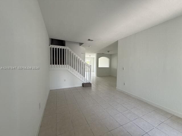 Open-concept interior featuring neutral tile flooring, white walls, a staircase with a white railing, and a decorative archway