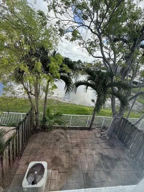 Paved patio featuring a water-front location, perimeter wood fencing, and mature trees