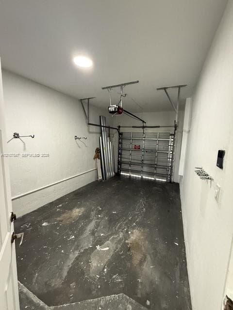 Enclosed garage featuring an automated overhead door system, ceiling-mounted lighting, and wall-mounted storage hardware