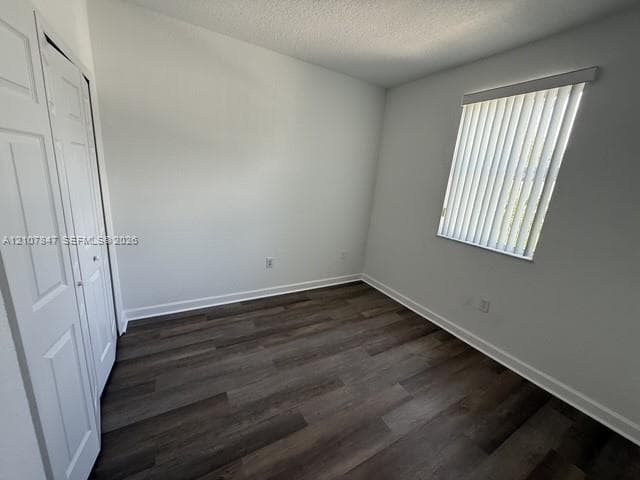 Neutral wall coloring, wood-finish flooring, and built-in closet with panel doors, featuring a window with vertical blinds